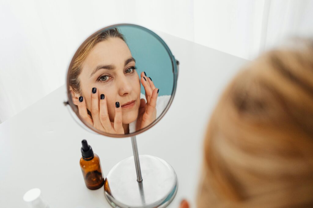 A woman applying a summer skincare routine in the bathroom mirror.