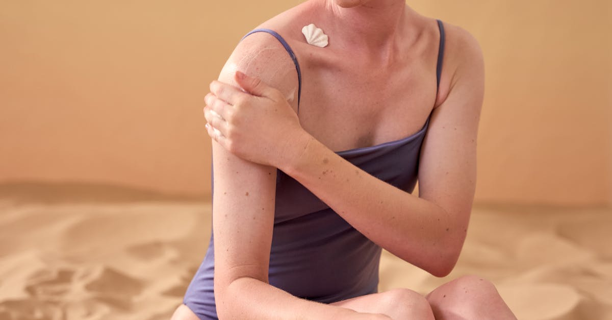 Caucasian woman applying sunscreen while sitting on sand, embodying skin protection and self-care.